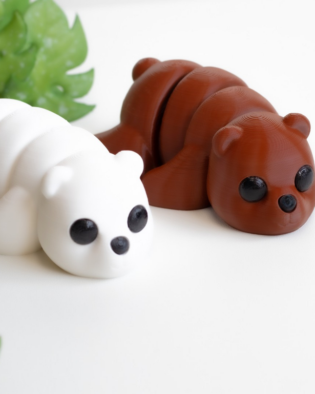 Two small animal figurines, one white and one brown, on a white surface with green leaves in the background.