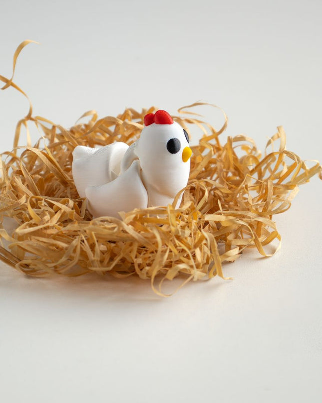 Small white chicken figurine with a red comb in a nest of straw on a light gray background