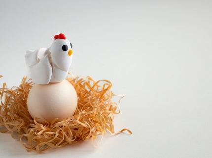 Small chicken figurine on a nest of straw with a white background
