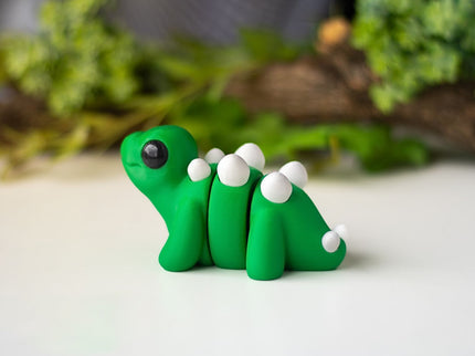 Green plastic stegosaurus figurine on a white surface with greenery in the background