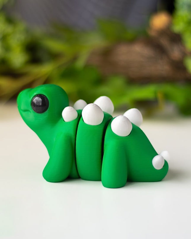 Green plastic stegosaurus figurine on a white surface with greenery in the background