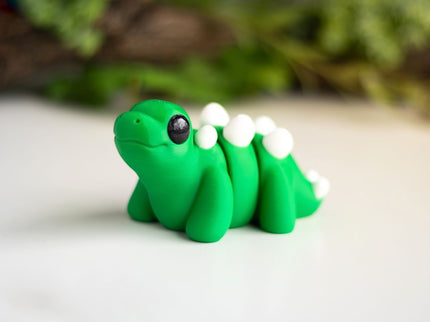 Green plastic stegosaurus figurine on a white surface with greenery in the background