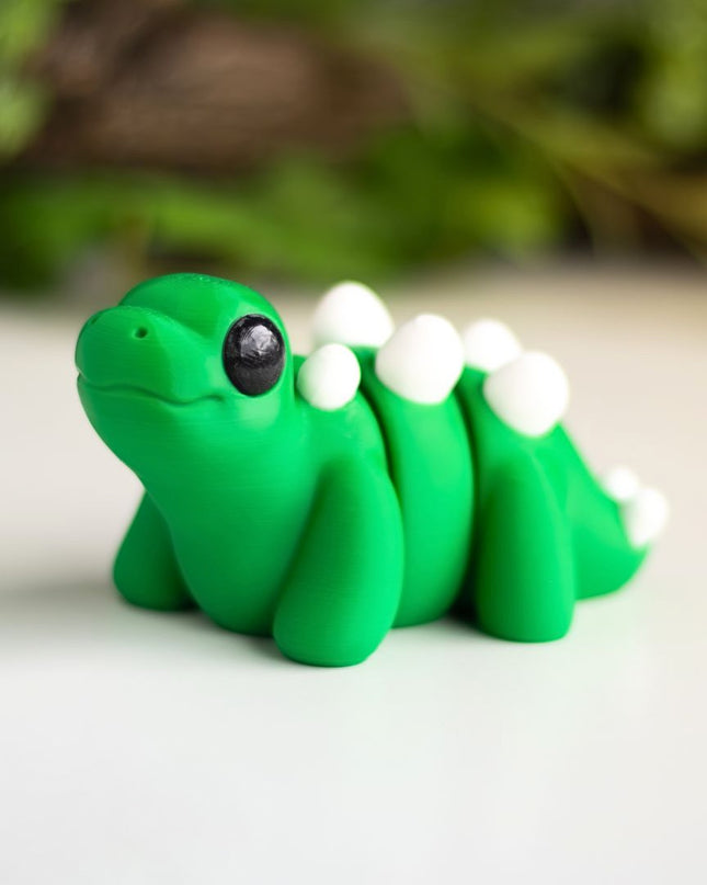 Green plastic stegosaurus figurine on a white surface with greenery in the background
