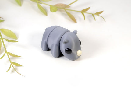 Small gray rhino figurine on a white background with green leaves