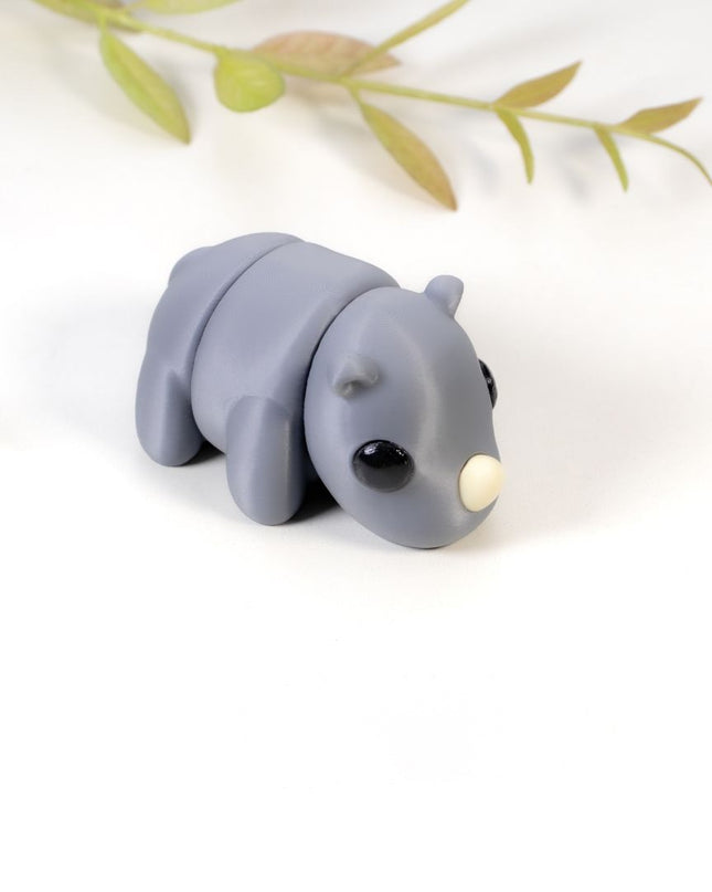 Small gray rhino figurine on a white background with green leaves
