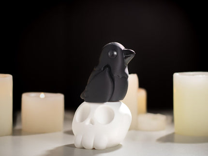Black raven toy sitting on a cartoon white skull with lit candles in the background