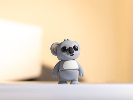 Small gray toy koala on a white surface with a blurred background
