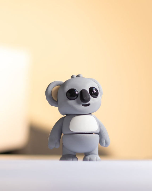 Small gray toy koala on a white surface with a blurred background