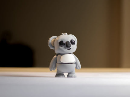 Small gray koala toy on a reflective surface with a blurred background