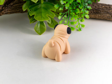 Small beige dog figurine on a white surface with green leaves in the background