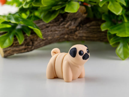 Small toy Pug on a white surface with green leaves in the background