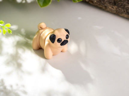 Small toy Pug dog figurine on a textured surface with greenery