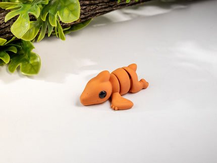 Small orange pterodactyl toy on a white surface with green leaves in the background