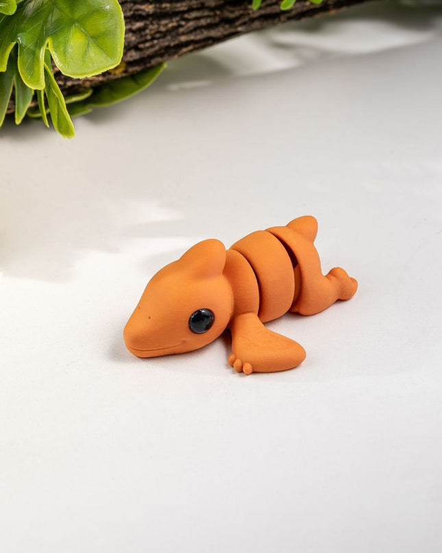 Small orange pterodactyl toy on a white surface with green leaves in the background