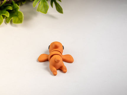 Small orange pterodactyl toy on a white surface with green leaves in the background