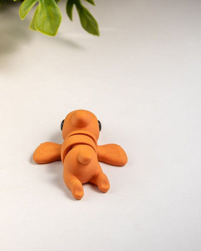 Small orange pterodactyl toy on a white surface with green leaves in the background