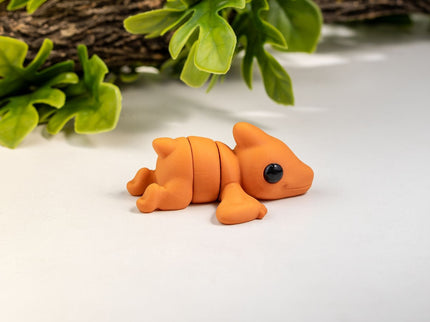 Small orange pterodactyl toy on a white surface with green leaves in the background