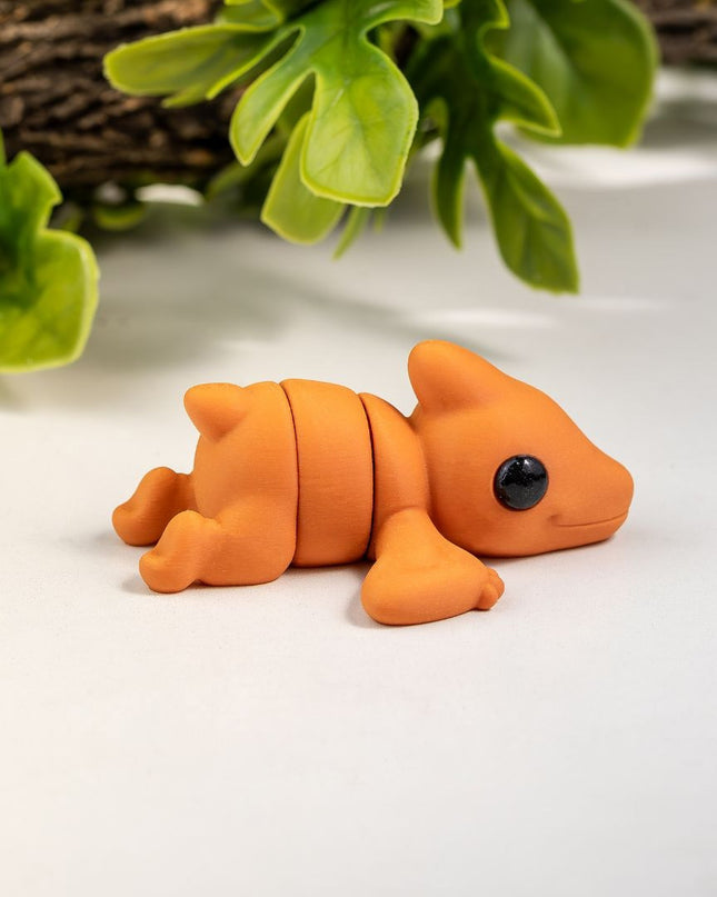 Small orange pterodactyl toy on a white surface with green leaves in the background