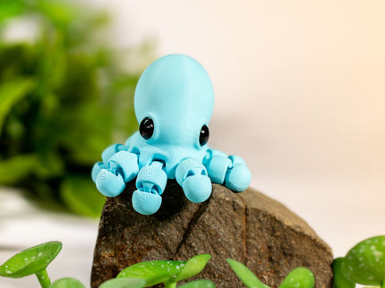 Small blue octopus figurine on a rock with green plants in the background
