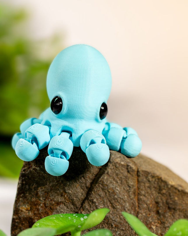 Small blue octopus figurine on a rock with green plants in the background