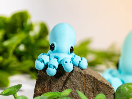 Small blue octopus figurine on a piece of wood with green leaves in the background