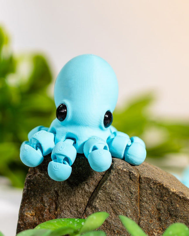 Small blue octopus figurine on a piece of wood with green leaves in the background