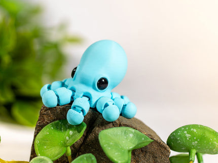 Small blue octopus figurine on a rock with green leaves