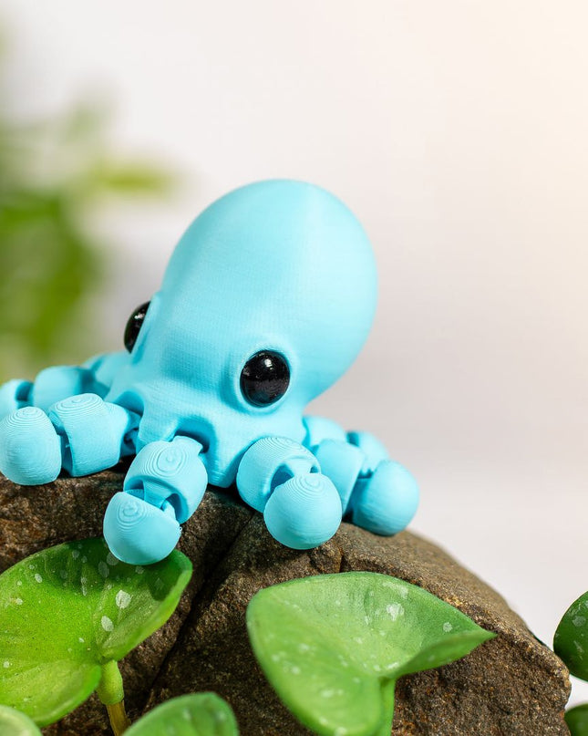 Small blue octopus figurine on a rock with green leaves