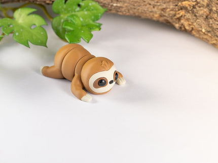 3d printed Sloth toy on a white surface with green leaves and wood in the background