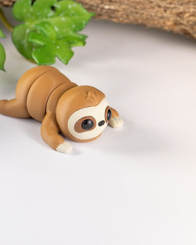 3d printed Sloth toy on a white surface with green leaves and wood in the background