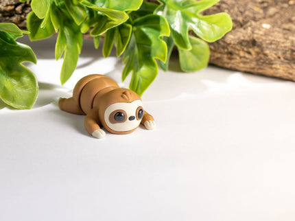 3d printed Sloth toy on a white surface with green leaves in the background