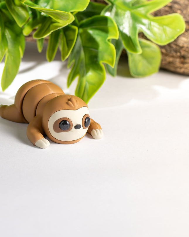 3d printed Sloth toy on a white surface with green leaves in the background
