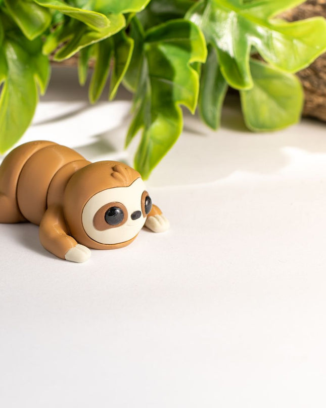 3d printed Toy sloth on a white surface with green leaves and wood in the background