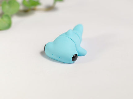 Small blue articulated hammerhead shark shaped toy on a light background with light green leaves.