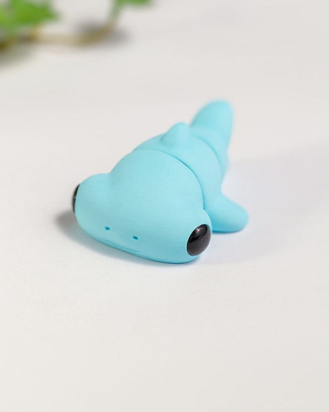 Small blue articulated hammerhead shark shaped toy on a light background with light green leaves.