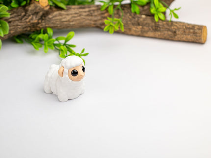 Small white figurine of a sheep toy  with green leaves and a branch in the background