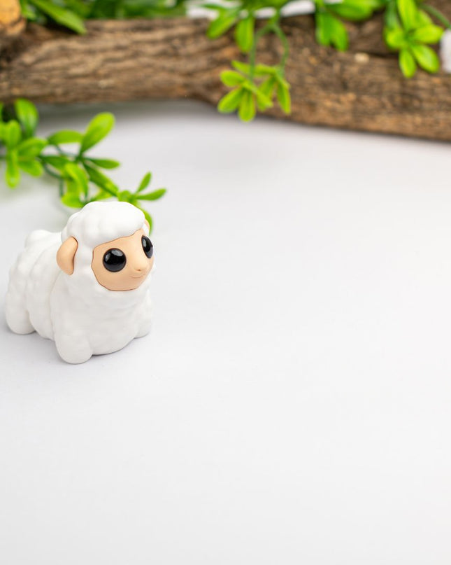 Small white figurine of a sheep toy  with green leaves and a branch in the background