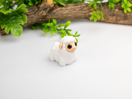 Small white sheep figurine with a brown face on a light gray background with green leaves and wood.