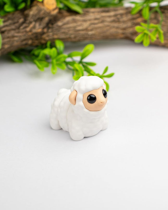 Small white sheep figurine with a brown face on a light gray background with green leaves and wood.