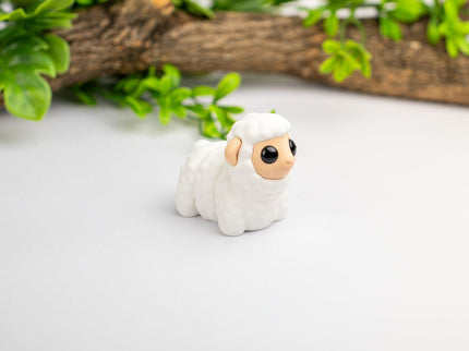 Small white figurine of a lamb on a light surface with greenery in the background