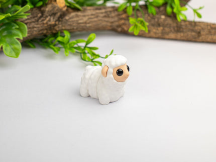 Small white figurine of a sheep on a light surface with greenery in the background