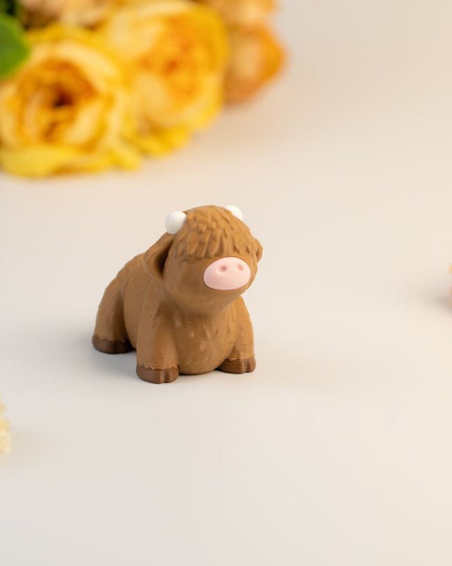 Small brown highland cow toy on a light surface with flowers in the background