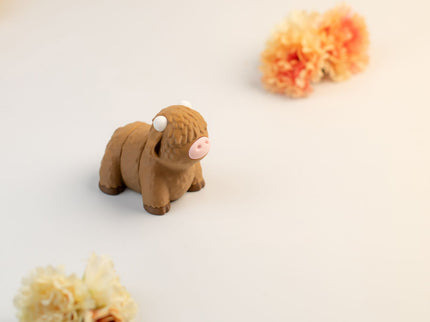 Small brown highland cow toy on a light surface with flowers in the background