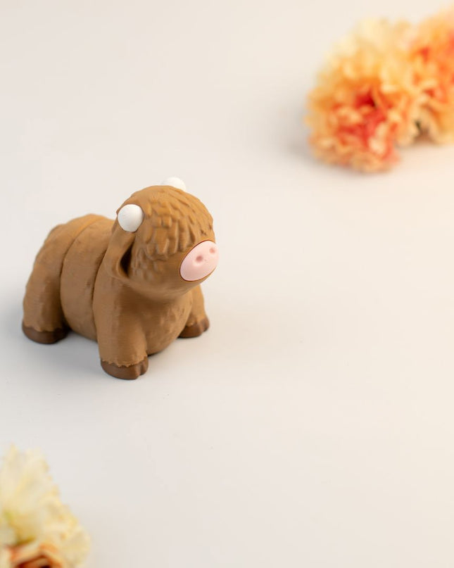 Small brown highland cow toy on a light surface with flowers in the background